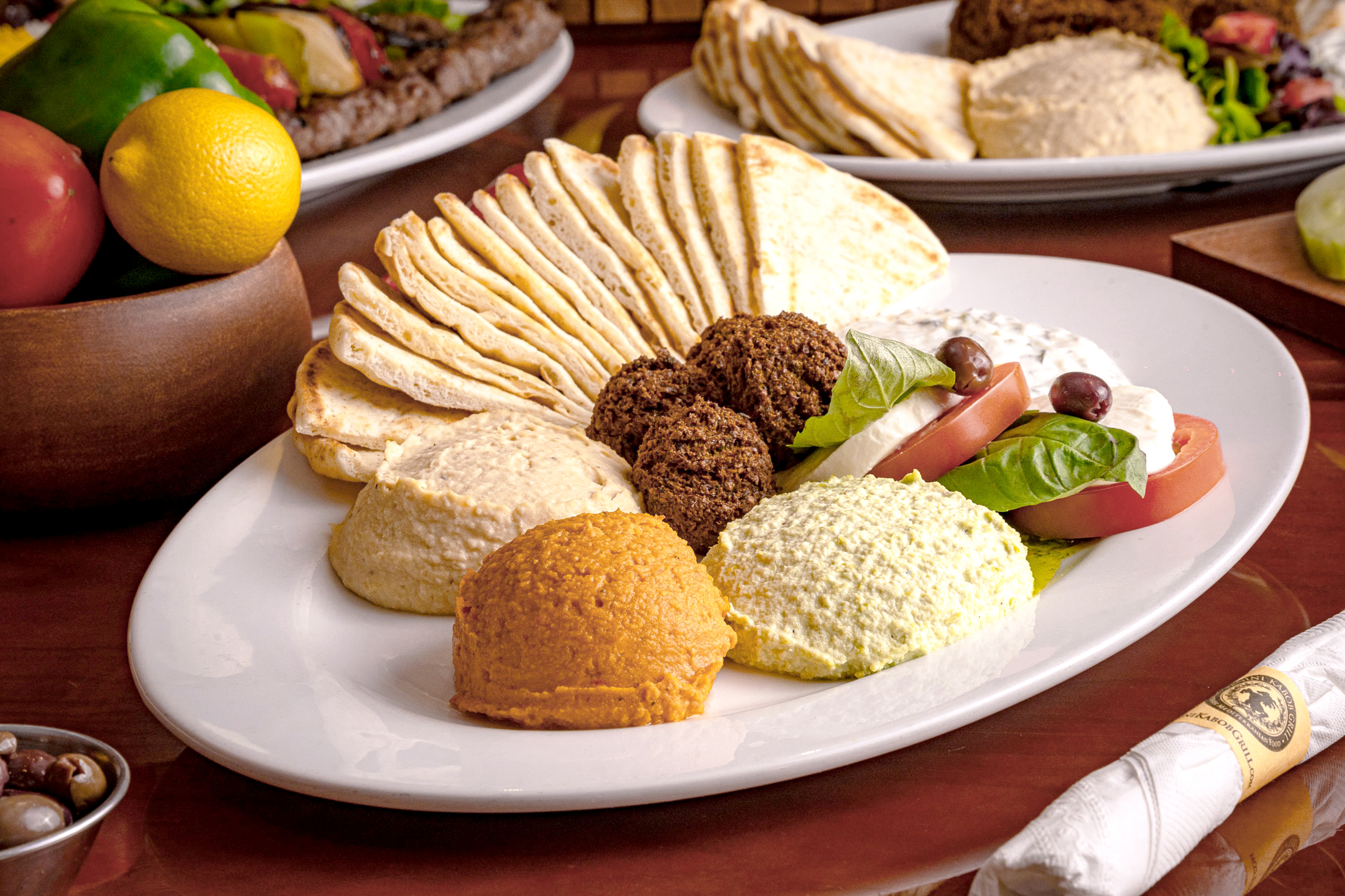 Panini Kabob Grill Mediterranean appetizer platter with falafel, warm pita bread, assortment of hummus dips, and fresh caprese salad