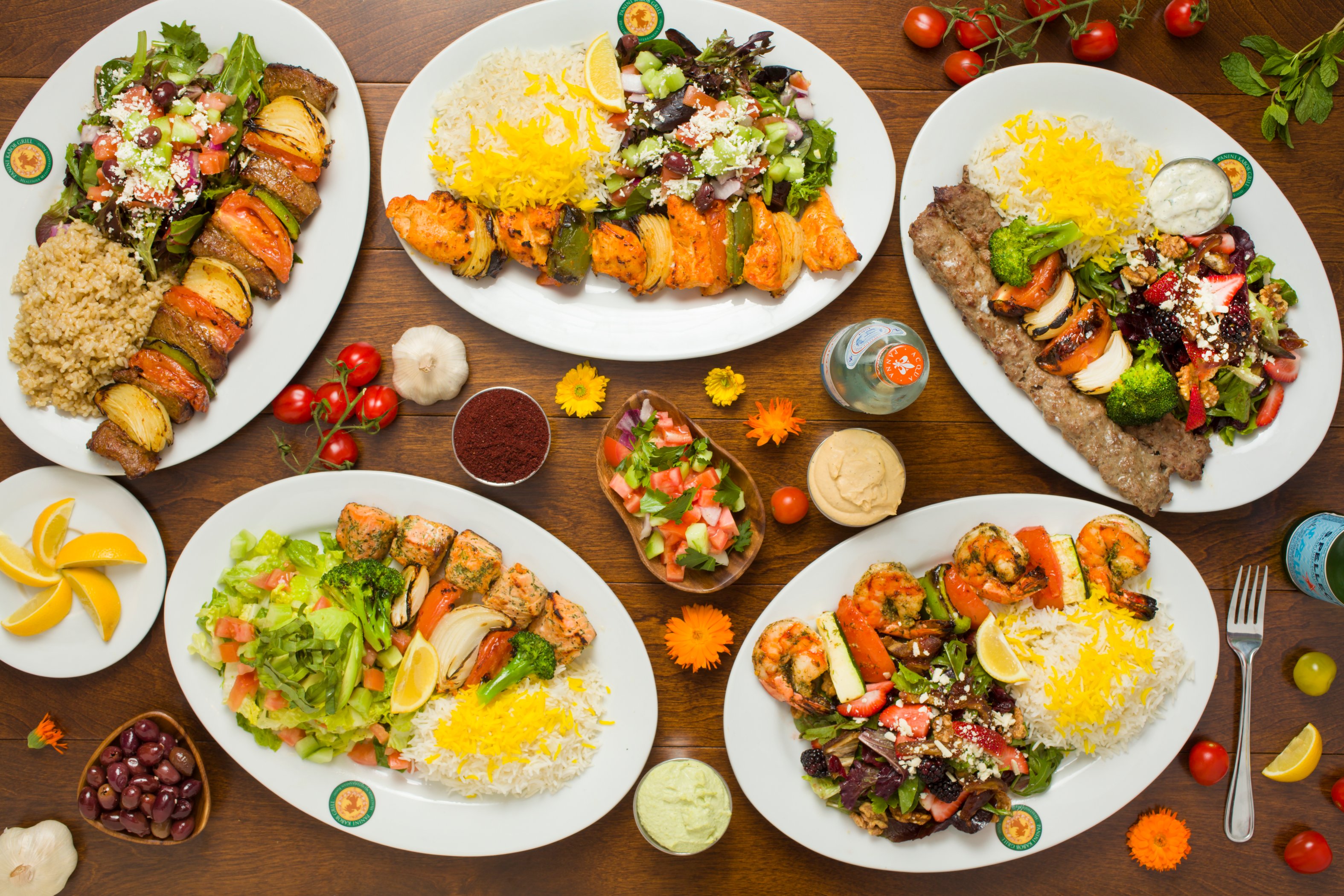 Overhead view of Panini Kabob Grill Mediterranean platters including chicken, beef koobideh, salmon, and shrimp kabobs served with saffron rice and fresh salads